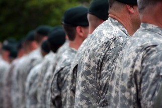 A group of military personnel in camouflage uniforms standing in line, viewed from behind.