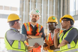 Group of construction workers wearing PPE on a job site and looking at a tablet computer