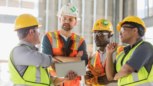 Group of construction workers wearing PPE on a job site and looking at a tablet computer