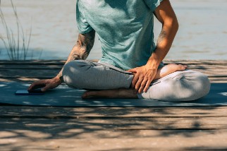 Man selecting a mindfulness app on his phone while sitting by a lake.jpg