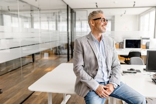 Safety professional man with glasses smiling and sitting on a desk