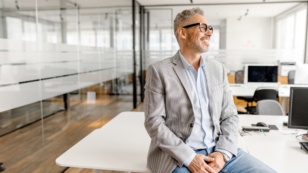 Safety professional man with glasses smiling and sitting on a desk