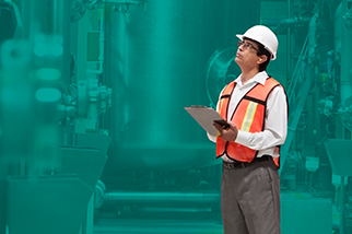 Safety professional man in safety vest and a hard hat holding a clipboard in front of a teal background
