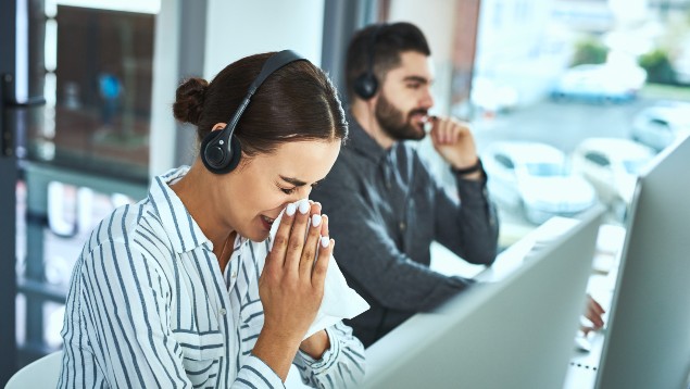 Woman in a call center sneezing beside her coworker