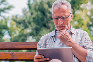 Mature man reading news on digital tablet on bench