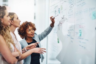 Three professionals collaborating and discussing notes on a whiteboard.