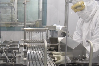 A person in protective lab gear operates machinery in a high-tech pharmaceutical manufacturing facility.