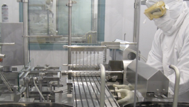 A person in protective lab gear operates machinery in a high-tech pharmaceutical manufacturing facility.