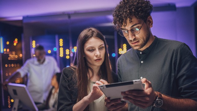 Male and female maintenance engineers examining data on digital tablet together in server room.